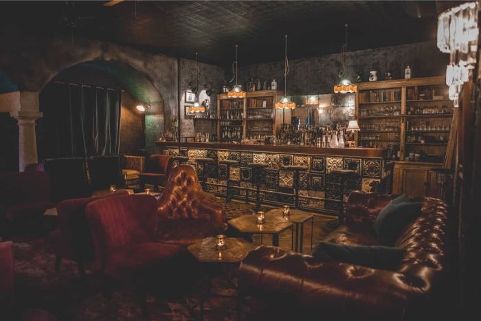 Michalská-cocktail-room-bar-kozene-kreslo-kozena-sedacka-zaclony-zavesy-barovy-pult-vintage-lustr-svicky-stůul-polstare-drinky-koktejly-lahve